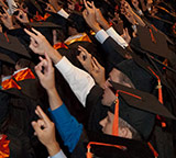 students at graduation flashing hookem horns sign